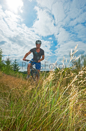 A young man on a mountain bike riding through grassy landscape, friend in the background