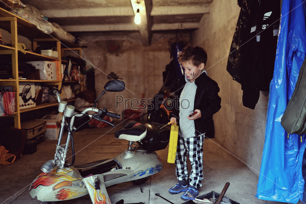 in the garage of a boy with dirty face and stylish hairstyle repairs moped