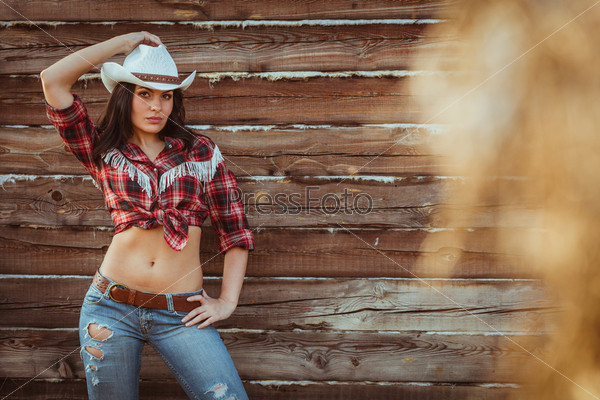 beautiful cowgirl style model posing on farmland near wood wall