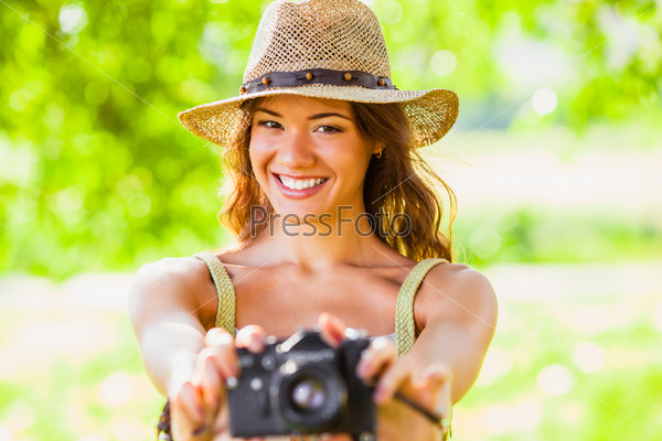 happy young girl wearing straw hat with vintage camera walking outdoors in the park, camera is out of focus