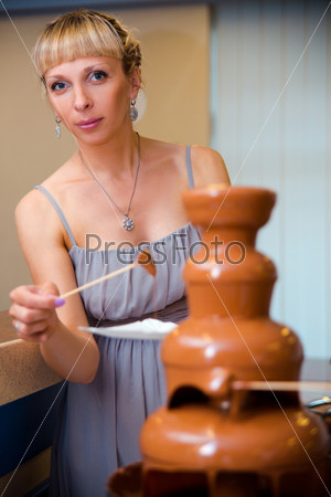 Beautiful young woman using chocolate fondue on gala dinner