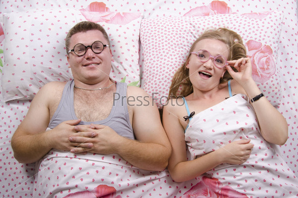 Young couple lying in bed. On each dressed round funny glasses. Top view