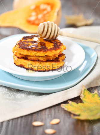 Pumpkin pancakes with honey on the wooden background