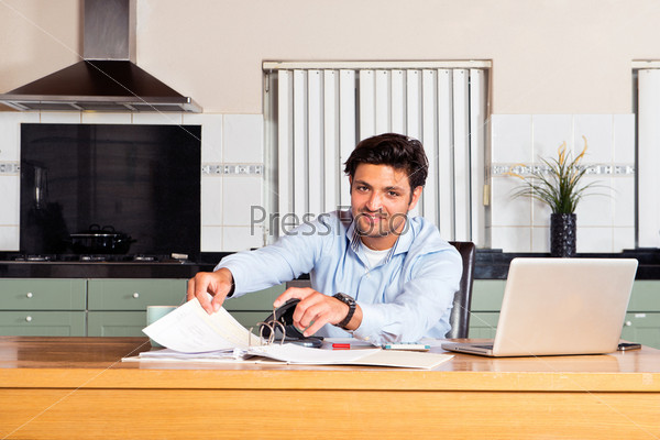 Handsome man filing paid giro cards and transaction forms in a binder whilst doing his personal administration getting his finances in order at the kitchen table