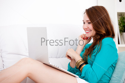 Smiling happy woman sitting on the sofa and using laptop at home