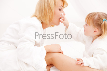 mother and daughter applying cream on mother\'s face on bed