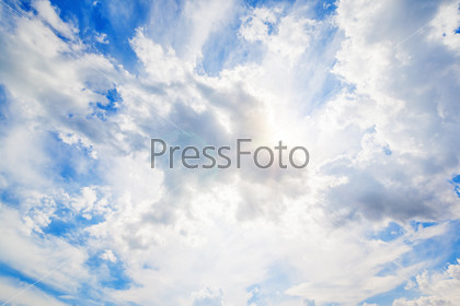 Sun in clouds with flare on blue sky
