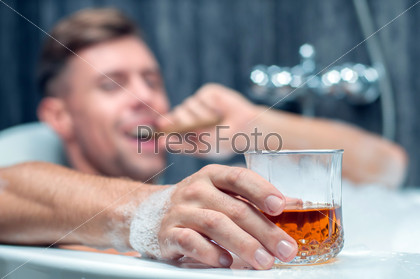 young man taking a bath, drinking whiskey and smoking cigar