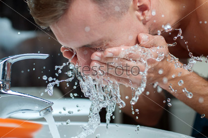 Bright caucasian man spraying water on his face after shaving in the bathroom at home