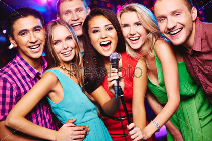 Portrait of happy girls and guys singing in microphone in the karaoke bar