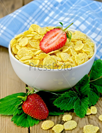 Corn flakes in bowl with strawberries on a board
