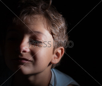 headshot of the boy in the dark, focused light on the one side, sad alone 7 years old