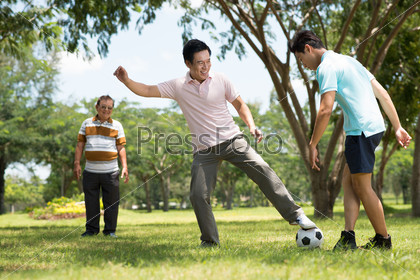 Father and his son playing football while the grandfather looking at them on the foreground