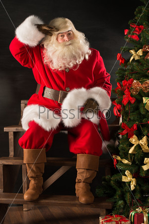 Authentic Santa Claus sitting near Christmas tree and looking tired after delivering all gifts to children