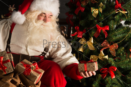 Santa Putting Gifts Under Christmas Tree In Dark Room