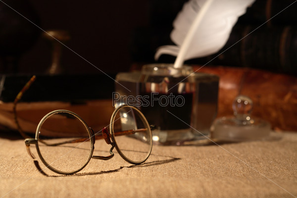 Vintage still life. Old spectacles closeup on dark background with inkstand and books