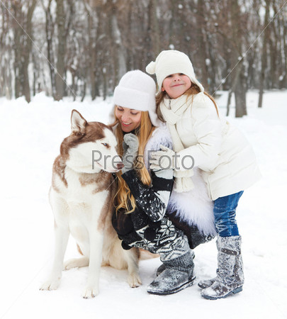 Happy young mother with daughter in the winter park with huskies dog