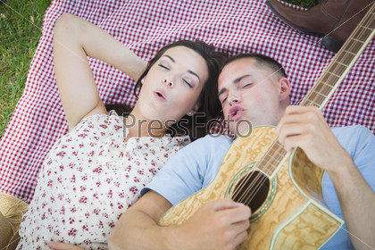 Happy Mixed Race Couple On Picnic Blanket at the Park Playing Guitar and Singing Songs.