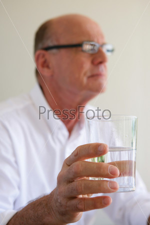 Elderly man taking medication with glass of water, stock photo