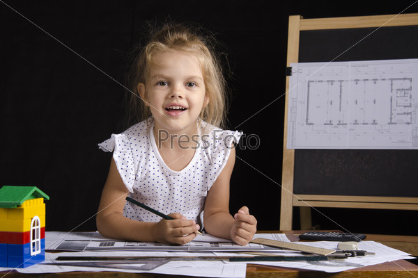 Улыбающаяся девочка смотрит в кадр за рабочим столом, играя в архитектора