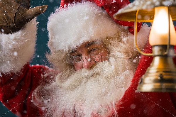 Santa Claus is holding a shining lantern while sneaking to his home outdoors at North Pole
