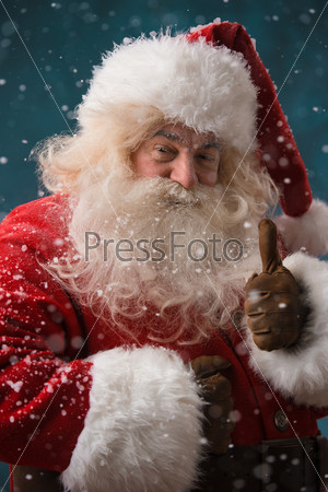 Santa Claus standing outdoors at snowfall at north pole and showing thumb up