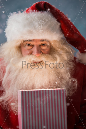 Portrait of happy Santa Claus opening gift box outdoors at North Pole. Magical light from box on his face