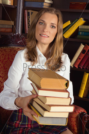 Portrait of blond girl sitting in chair and holding stack of books in library