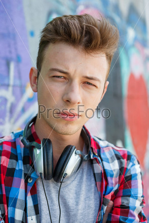Close-up portrait of happy teens boy with headphones near painted wall listening to music. Vertical view