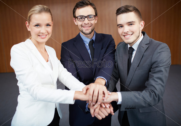 Group of business partners making pile of hands and looking at camera with smiles