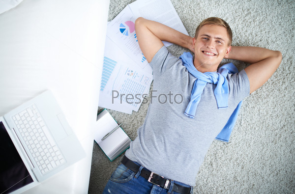Above view of young guy in casual lying on the floor and looking at camera with smile, stock photo