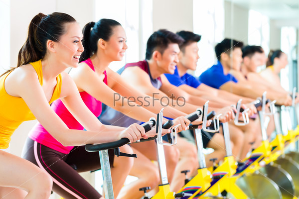 Chinese Asian sport group of men and women in fitness club or gym exercising on bikes