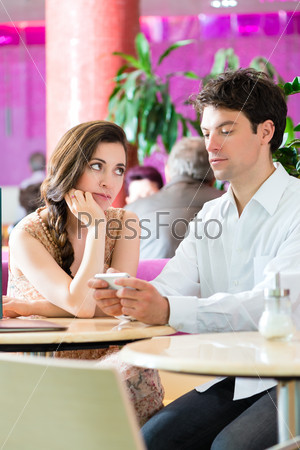 Couple in a cafe spends leisure time together, she is angry because he is busy on the phone