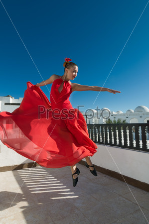 Attractive flamenco dancer wearing traditional red dress with flower in her hair jumping high