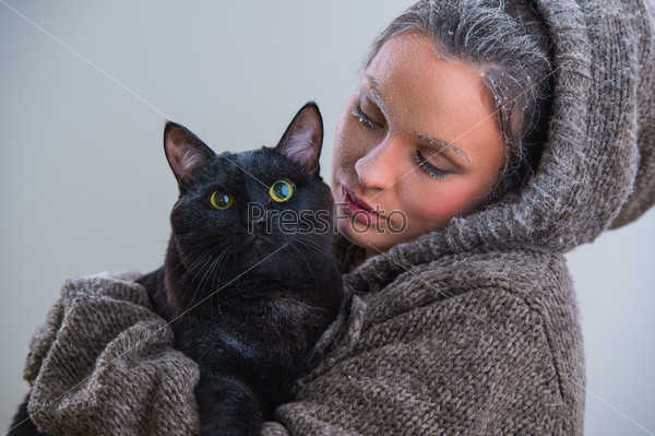 Winter portrait of young kind woman holding big black cat. Frost and snow on them