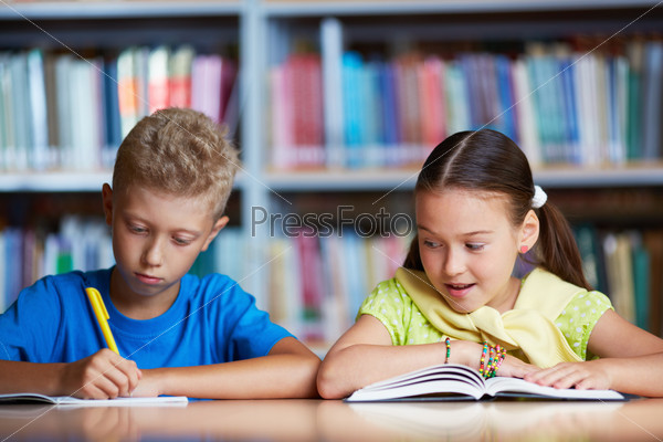 Portrait of diligent schoolchildren reading together in library