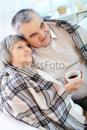 Portrait of serene senior couple wrapped in plaid having rest at home