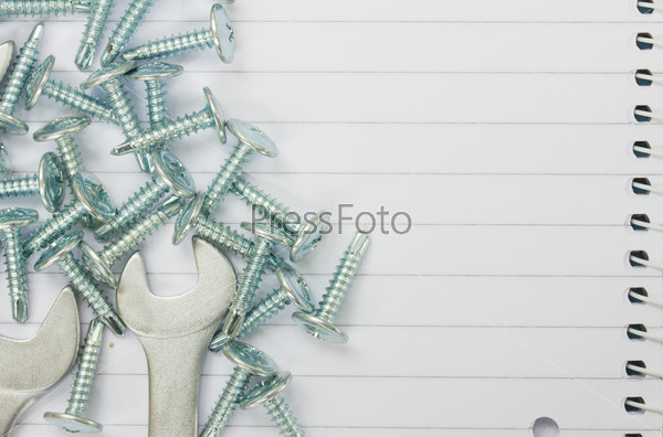 disassembled screws and wrenches on ruled paper background with yellow tape an copy space