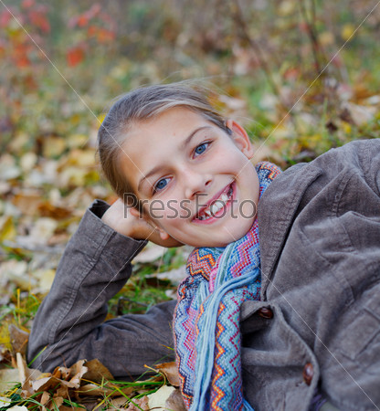 Portrait of happy girl lying on autumnal ground covered with dry leaves
