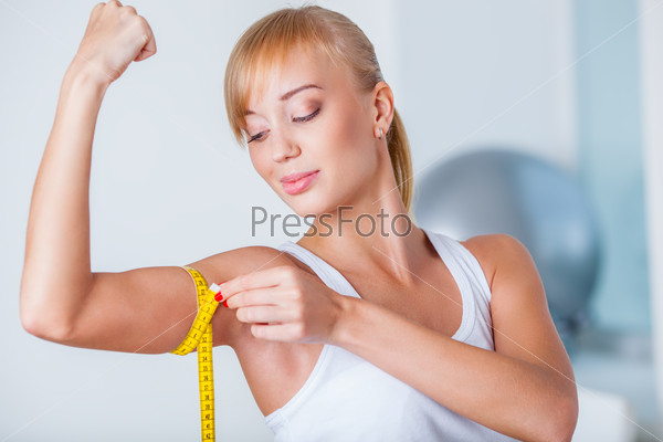 young beautiful blonde woman measuring her biceps with tape