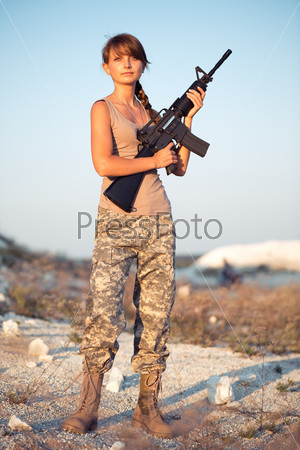 Young beautiful female soldier dressed in a camouflage with a gun in the location