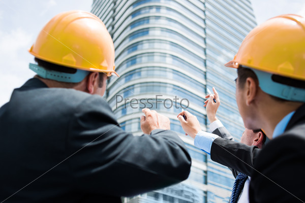 Back view of professional engineers pointing at the modern building on the foreground
