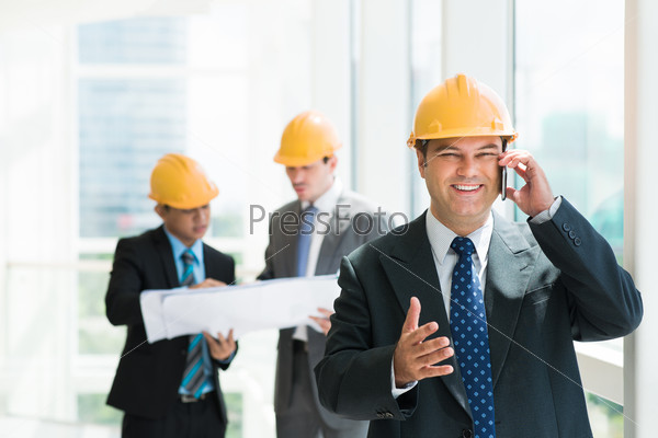 Portrait of a cheerful construction worker talking by phone and looking at camera on the foreground