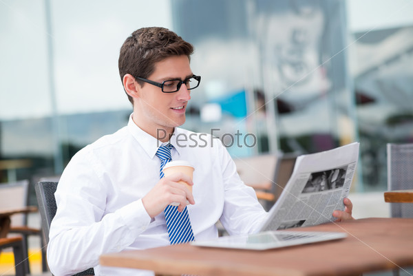 Copy-spaced image of a young businessman drinking coffee while reading the newspaper at a cafe on the foreground