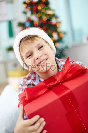 Portrait of cheerful boy with big red giftbox looking at camera on Christmas evening