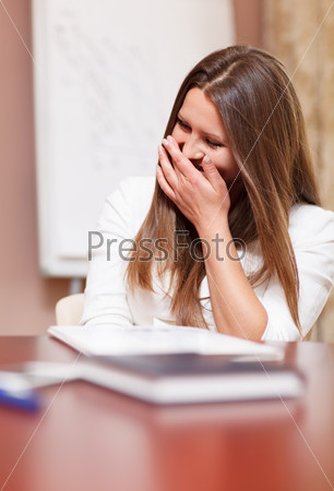 Businesswoman laughing in a meeting trying to stifle her laughter behind her hand