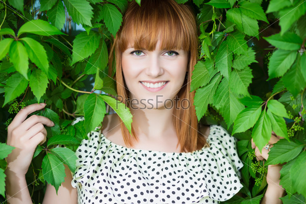 Portrait of pretty smiling redhead woman posing in green leaves