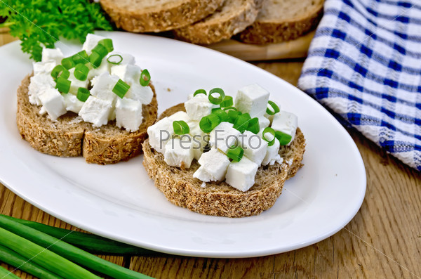 Slices of bread with feta cheese and chives on a plate, parsley, napkin on a wooden board