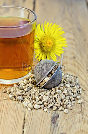 Metal sieve with elecampane root, fresh yellow flower elecampane, tea in glass mug on a background of wooden boards