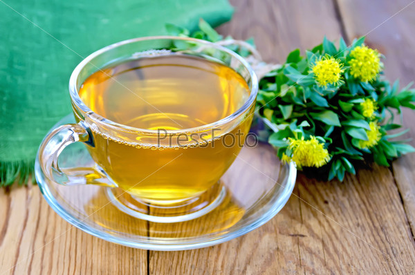 Healing herbal tea in a glass cup, a bouquet of flowers Rhodiola rosea, green napkin on a background of wooden boards